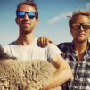 Two hot guys in sunglasses holding a goat.