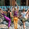 Three yogis standing before a sign that says 'wanderlust' striking a crane pose