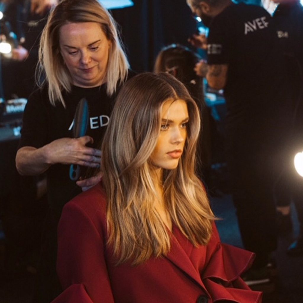 Woman sitting while Aveda beauty professional examines hair