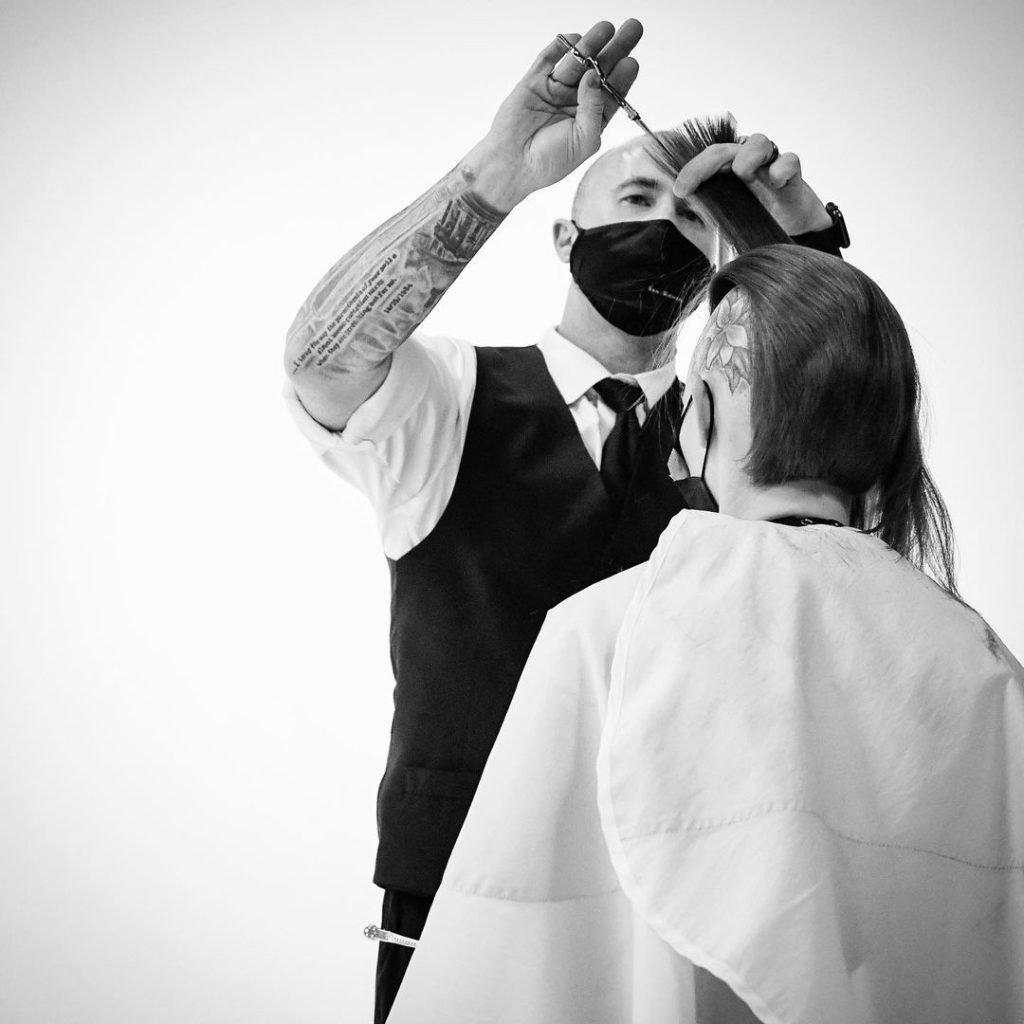 Beautician in face mask trimming client's hair